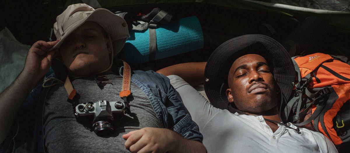 From above of young multiracial best friends with closed eyes sleeping on backpacks during summer trip
