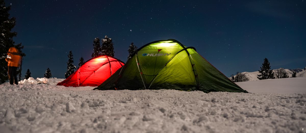 Two tents illuminated at night, set on a snowy landscape beneath a clear starry sky.