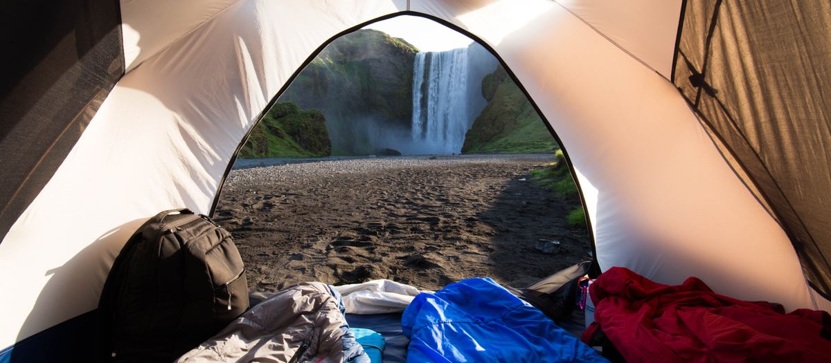View from a camping tent interior looking at a scenic waterfall in a wilderness setting.