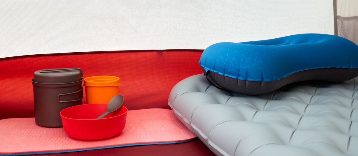 Inside a tent with inflatable pillow, cookware, and sleeping pad, ideal for camping.
